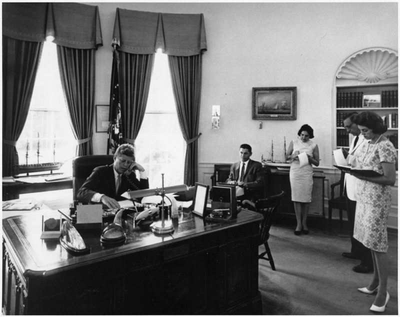 President Kennedy addresses AMVETS Convention in New York City by telephone.  President Kennedy, assistants. White House, Oval Office.